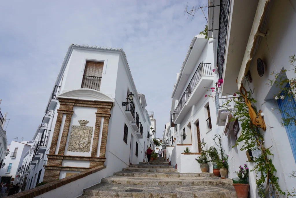 Callejón empedrado del Albaicín con casas blancas y macetas y la Alhambra asomando al fondo