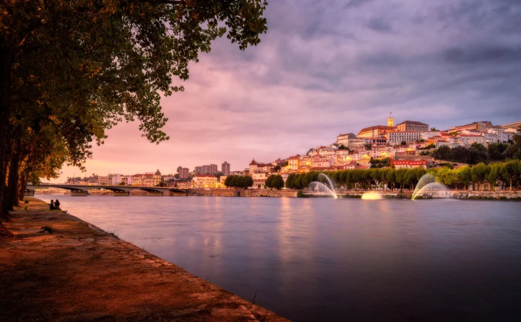 Vista de la Alta de Coimbra con la torre de la universidad sobre el río Mondego al atardecer