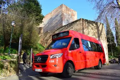 Minibús urbano rojo recorriendo la Carrera del Darro junto al río en Granada