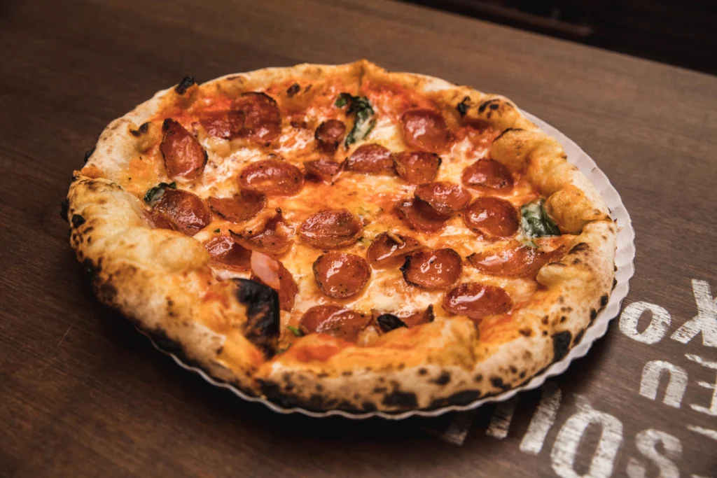 Porción de pizza neoyorquina doblada al medio frente al mostrador de una pizzería de barrio