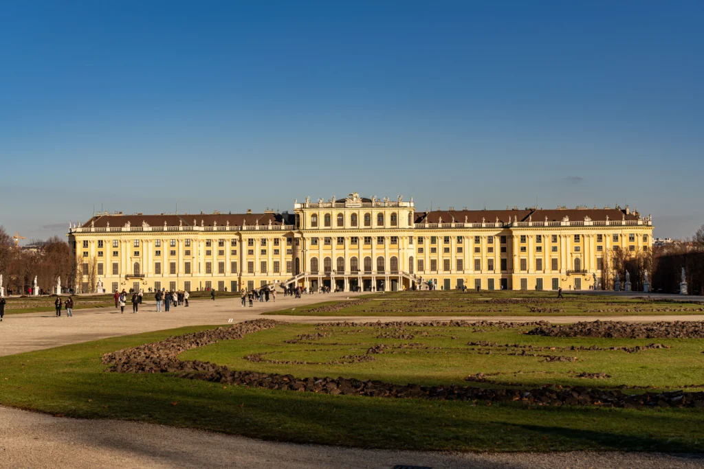 Fachada amarilla del Palacio de Schönbrunn vista desde los jardines con visitantes paseando