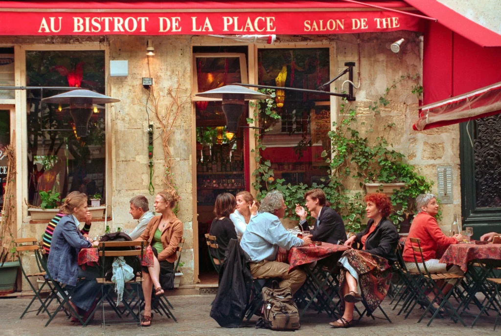 Terraza de un bistró de París con mesas de mimbre y gente almorzando en la vereda